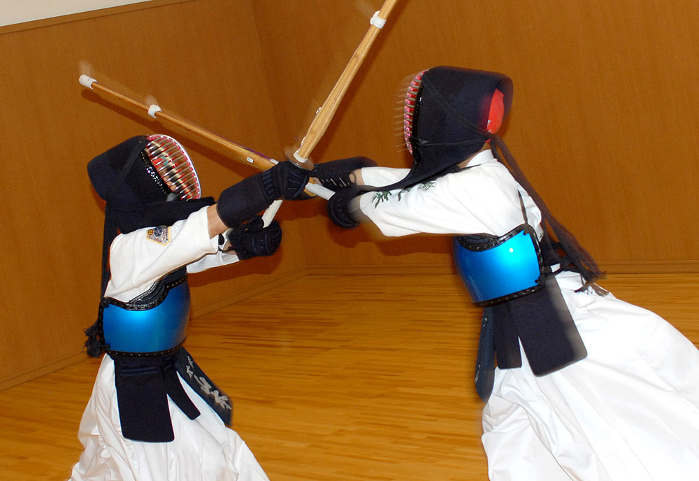 Two children engage in kendo training together, they are part of the same dojo and are practicing simultaneous striking.