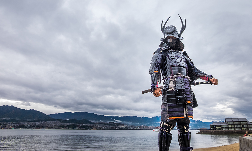 An armor-wearing Samurai standing in front to Itsukushima Jinja shrine